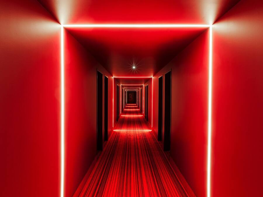 Un pasillo iluminado en rojo con suelo alfombrado y paredes, que conduce a una lámpara en forma de estrella en el techo.