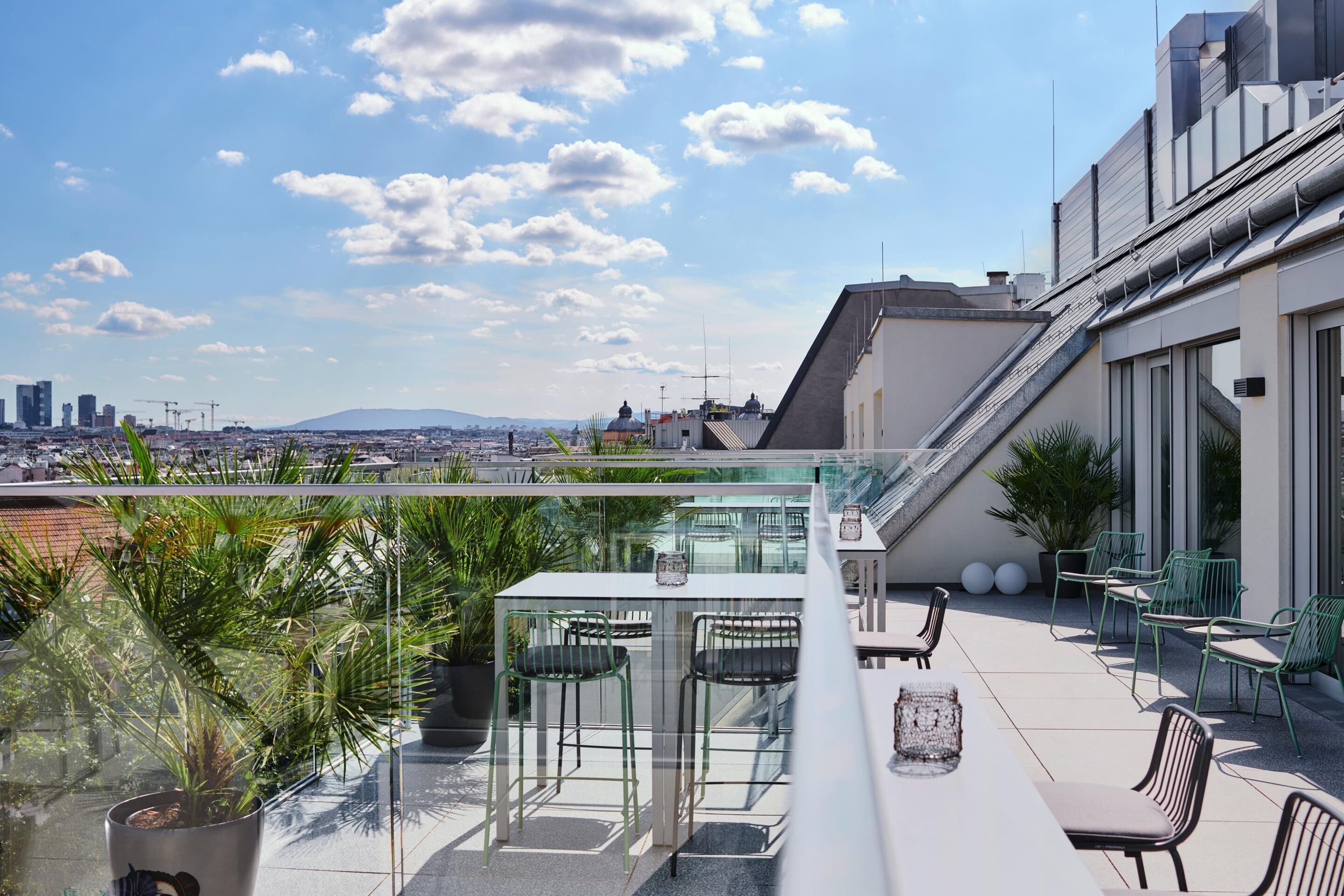 Eine Dachterrasse mit Glastisch und Stühlen, Topfpflanzen und Blick auf die Stadt.