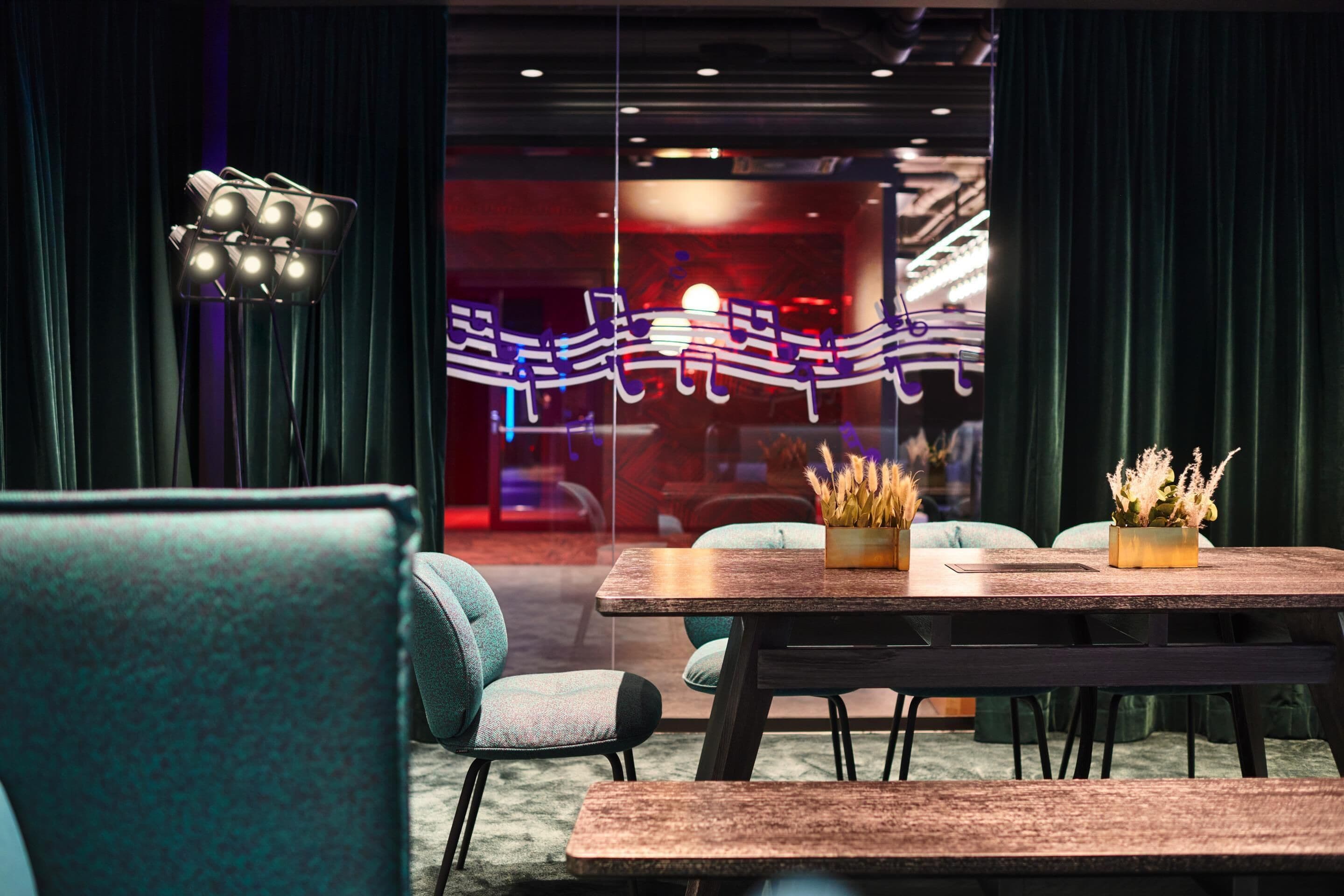 A modern conference room with a wooden table, teal chairs, and a decorative light fixture.