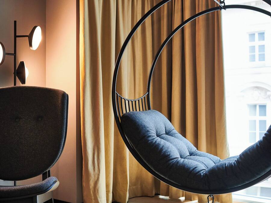 Una habitación moderna con una silla colgante, un escritorio y un ventanal con cortinas.