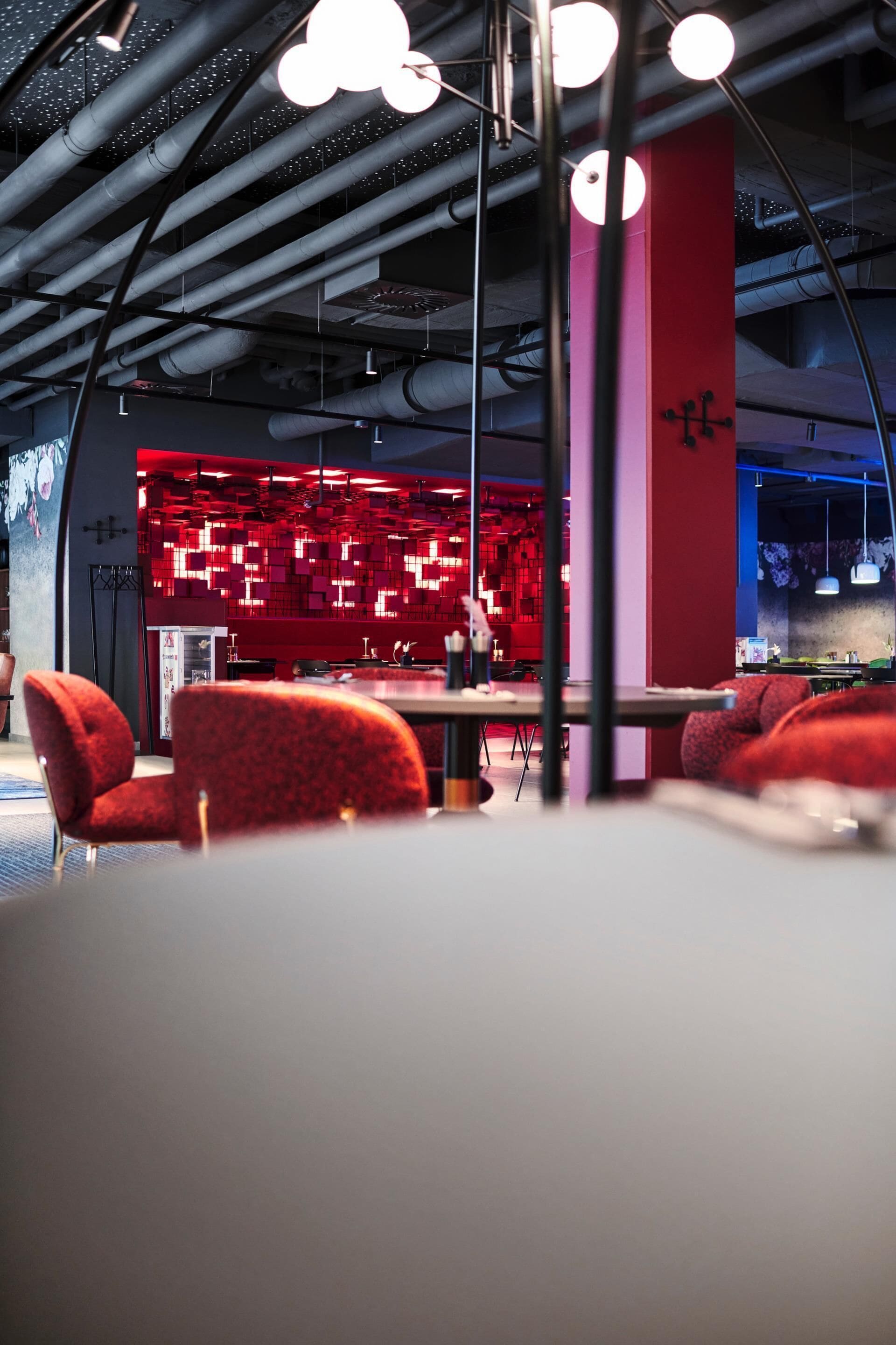 Un interno moderno con un'area salotto rossa, un bar con pannelli rossi illuminati e condotti a vista sul soffitto.