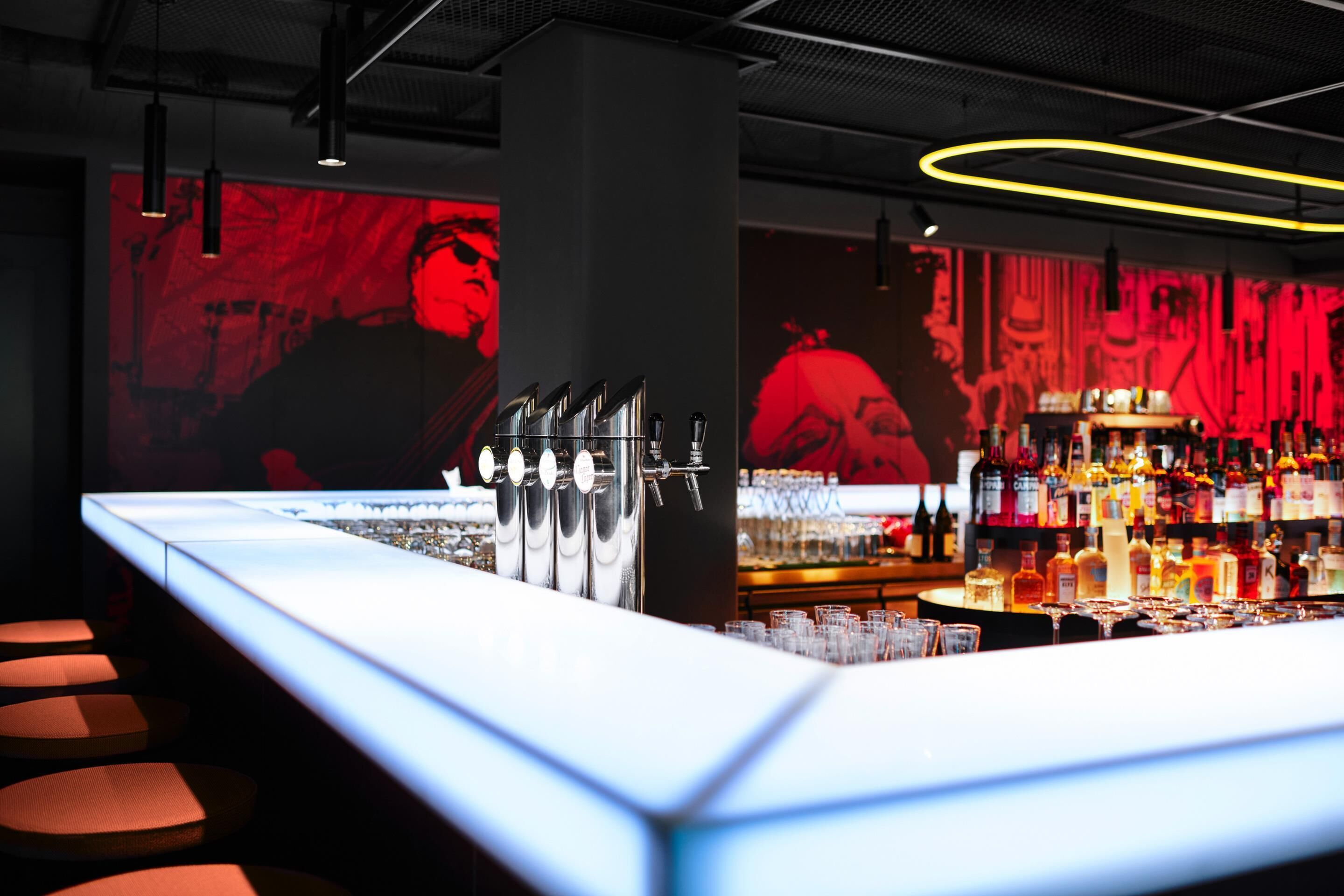 Una zona de bar con una barra alargada, múltiples grifos y una gran variedad de botellas y vasos.