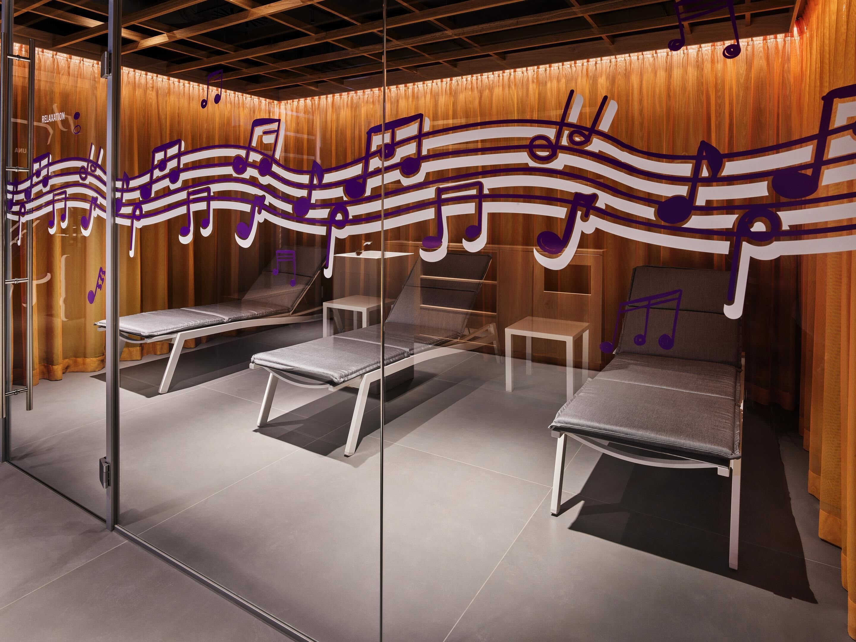 A room with three reclining chairs, a small table, and a wall with a musical note design.