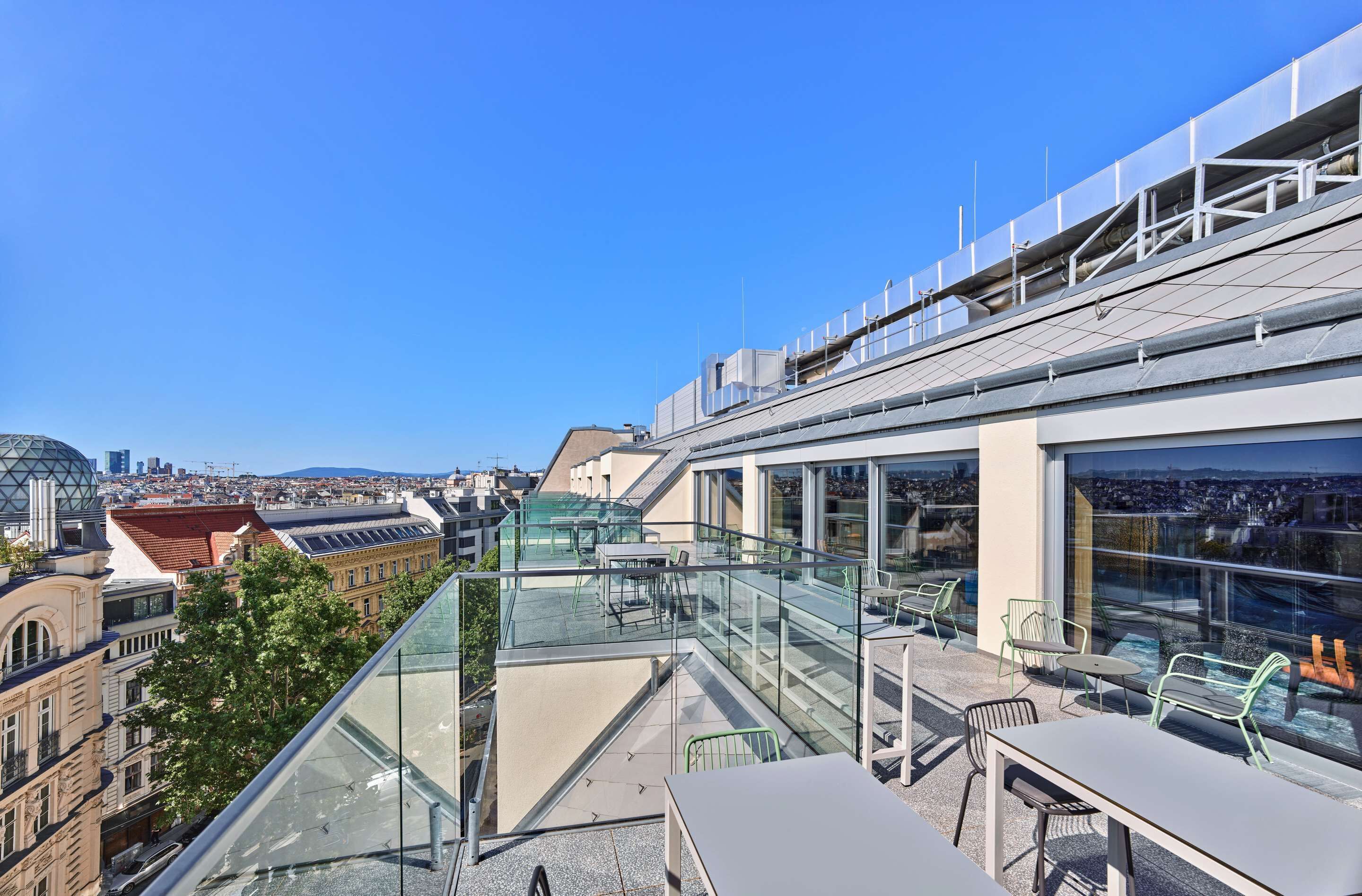 A rooftop terrace with glass railings, outdoor seating, and a city view.