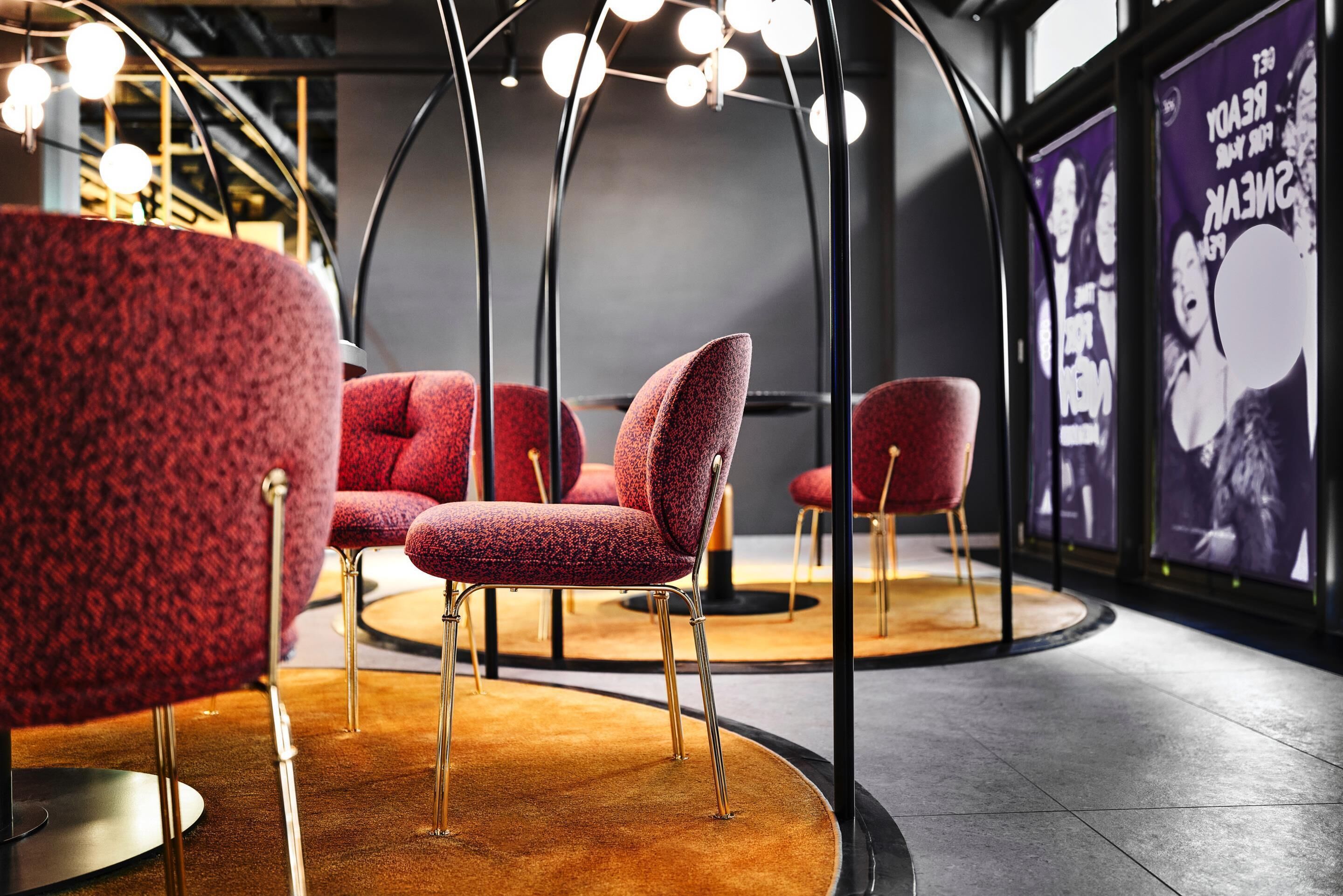 Um interior moderno com cadeiras estofadas em vermelho, uma luminária de teto singular e um pôster na parede.