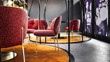 Um interior moderno com cadeiras estofadas em vermelho, uma luminária de teto singular e um pôster na parede.