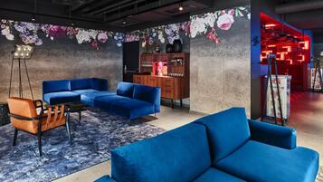 Ein moderner Lounge-Bereich mit blauen Sofas, einer Holzkommode und einer Wand mit floralen Mustern.