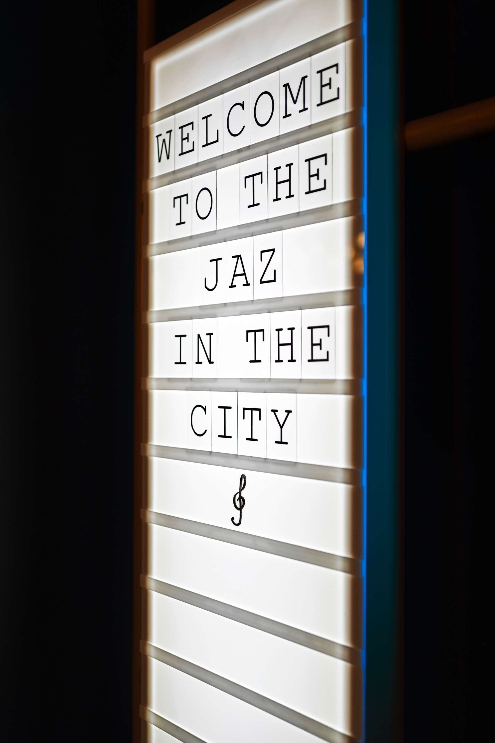 Een bord met de tekst 'WELCOME TO THE JAZZ IN THE CITY' en een muzieknoot symbool.