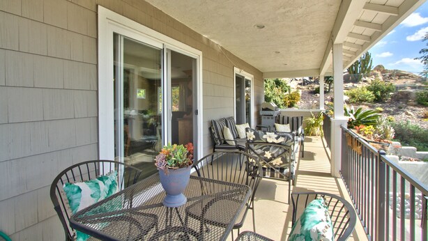 A covered patio with a table and chairs, a potted plant, and a view of the surrounding landscape. - Hilltop Comforts (Fallbrook)