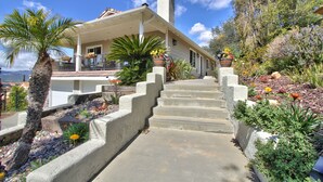 A house with a covered porch, concrete steps, and a garden with various plants and flowers. - Hilltop Comforts (Fallbrook)