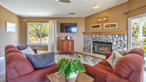 A living room with a fireplace, a television, and a large window with curtains. - Hilltop Comforts (Fallbrook)