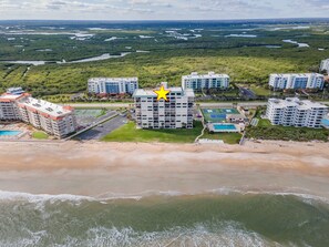 An aerial view of a coastal hotel complex with multiple buildings, a beachfront, and a large body of water. - Direct Oceanfront Views from Luxury Condo in Southwind Complex! (New Smyrna Beach)