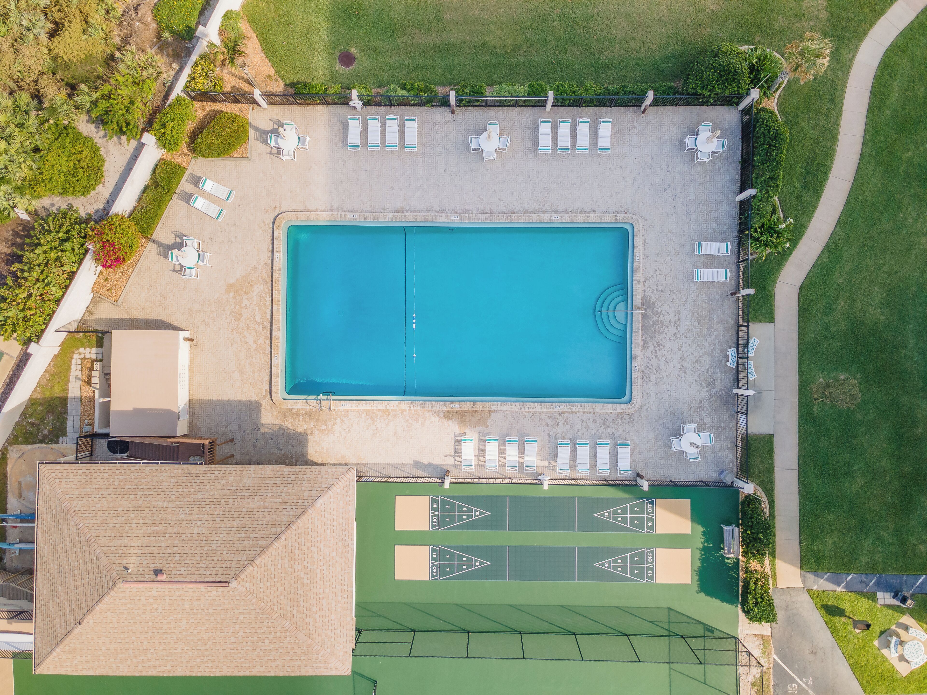 Vista aérea de una zona de piscina con sillones de descanso y una cancha de juego para paletas.