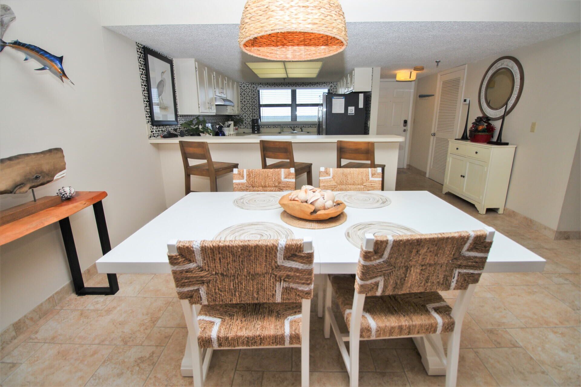 A dining area with a white table and four chairs with woven seat backs.