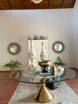 Cozy space with a glass-top table, white cabinet, and patterned cushions, complemented by decorative mirrors and potted plants.