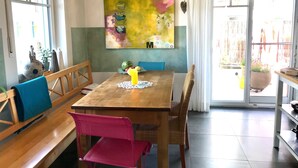 Zona pranzo con tavolo in legno, panche e sedie. Sopra il tavolo, un grande quadro appeso al muro.