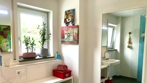 Un bagno con finestra, lavandino, specchio e mensole con asciugamani e articoli da toilette.