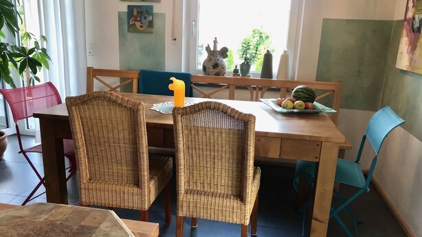 Zona pranzo con sedie in vimini, un tavolo di legno e un piatto di frutta.