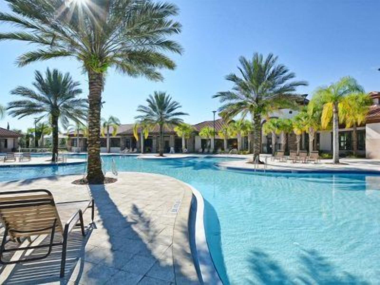 A swimming pool with palm trees, lounge chairs, and a clear sky.