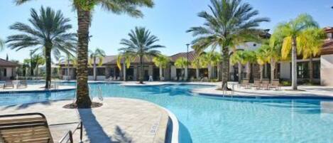 A swimming pool with palm trees, lounge chairs, and a clear sky.