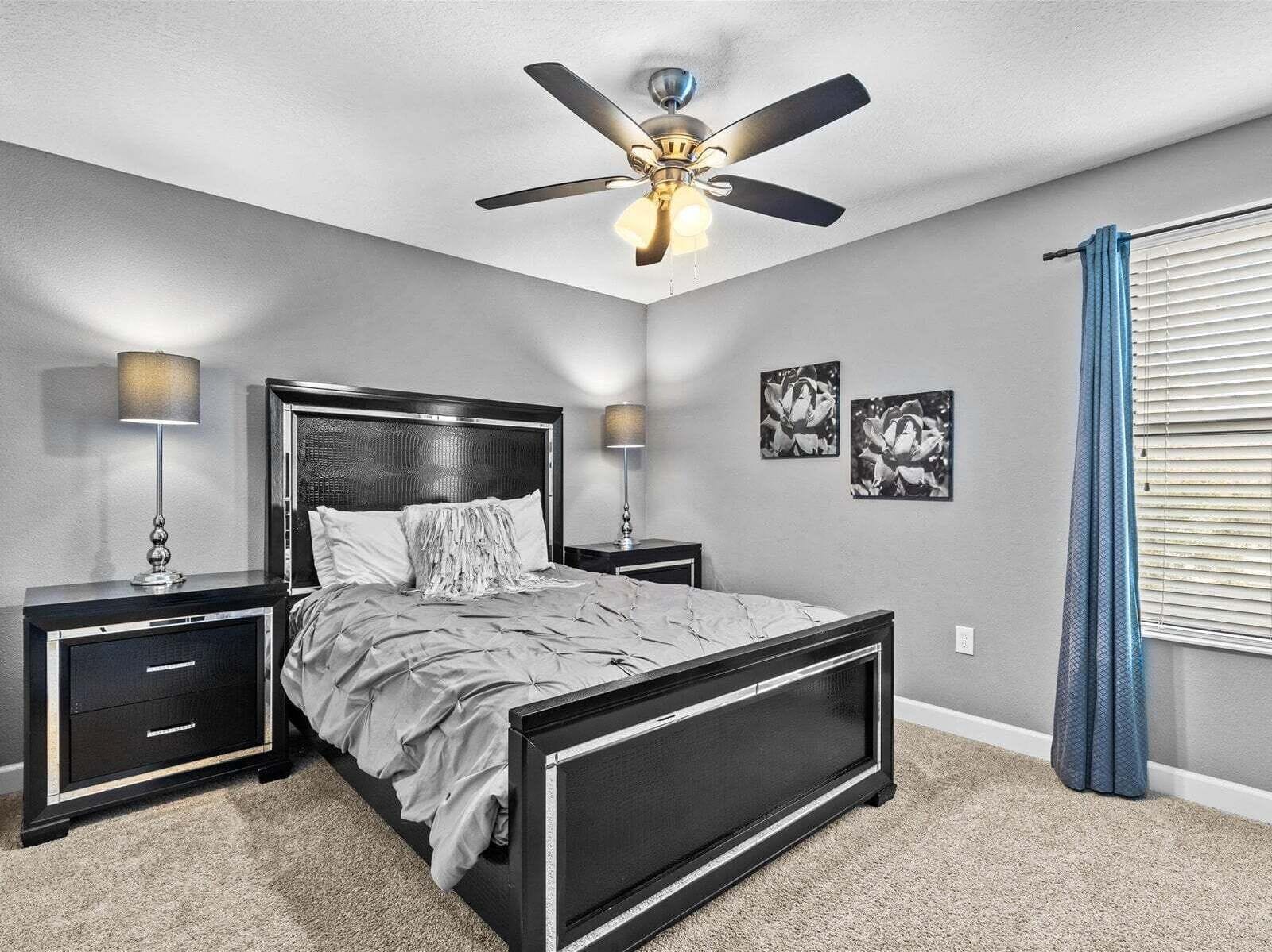 A bedroom with a bed, two bedside tables, a ceiling fan, and wall art.