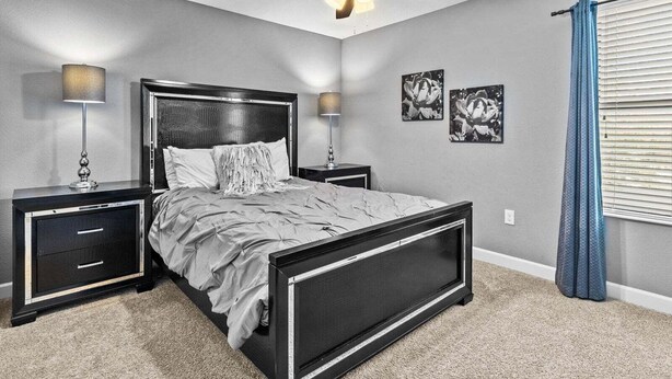 A bedroom with a bed, two bedside tables, a ceiling fan, and wall art. - 6BR Solterra Pool Home | Jacuzzi, Game Room, BBQ & 2 King Suites (Davenport)