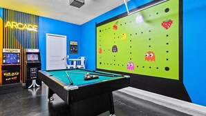 A pool table with a green felt surface, two Pac-Man arcade machines, and a wall with a green screen displaying pixelated ghosts. - 6BR Solterra Pool Home | Jacuzzi, Game Room, BBQ & 2 King Suites (Davenport)