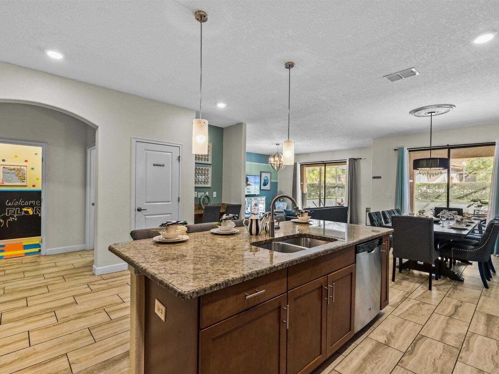 A modern kitchen with a granite countertop, stainless steel sink, and overhead pendant lighting.
