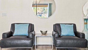 A room with two leather armchairs, a small side table, a mirror on the wall, and a vase with white feathers. - 6BR Solterra Pool Home | Jacuzzi, Game Room, BBQ & 2 King Suites (Davenport)