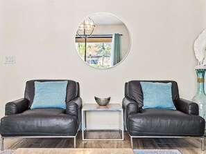 A room with two leather armchairs, a small side table, a mirror on the wall, and a vase with white feathers. - 6BR Solterra Pool Home | Jacuzzi, Game Room, BBQ & 2 King Suites (Davenport)