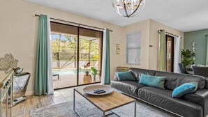 A living room with a sofa, coffee table, and a view of a pool. - 6BR Solterra Pool Home | Jacuzzi, Game Room, BBQ & 2 King Suites (Davenport)