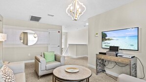 A living room with a flat-screen TV, a round coffee table, a sofa, a chandelier, and a fireplace. - 6BR Solterra Pool Home | Jacuzzi, Game Room, BBQ & 2 King Suites (Davenport)