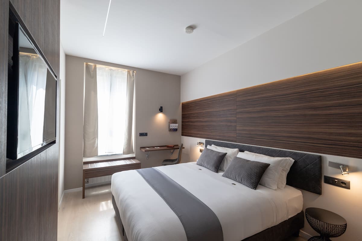 A modern bedroom with a large bed, bedside tables, a bench, and a TV.
