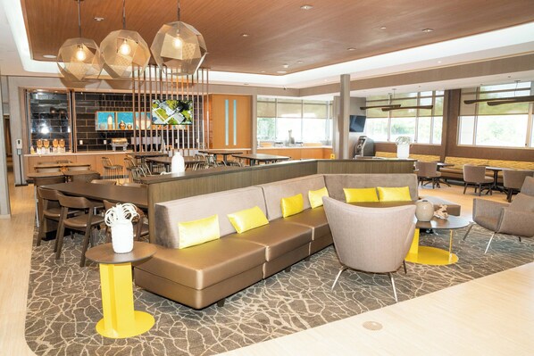Un hall d’hôtel moderne doté d’un espace salon, d’un bar et de grandes fenêtres.