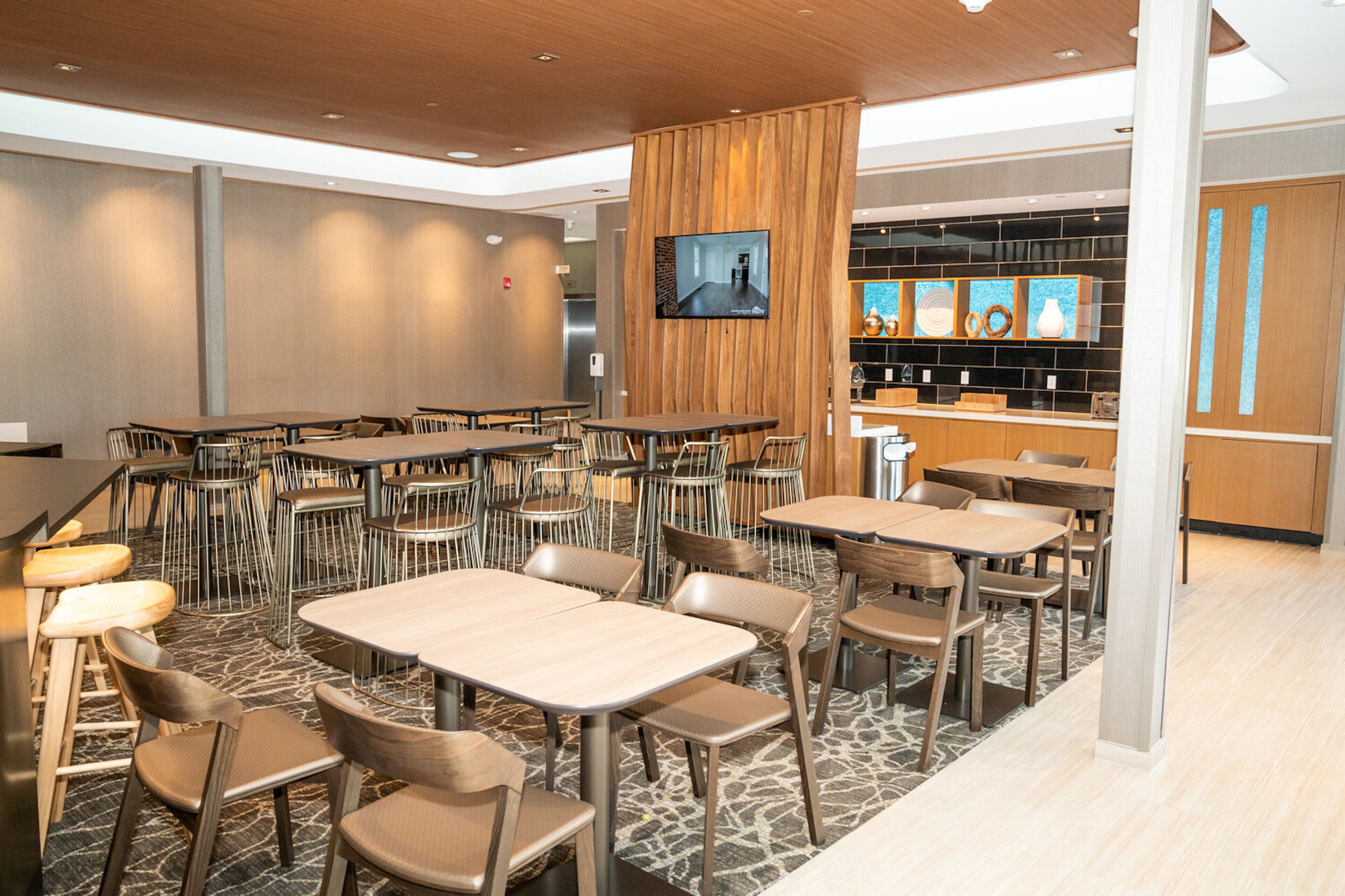 Ein modernes Restaurant mit mehreren Tischen, Stühlen, einem Fernsehbildschirm und einer Bar.
