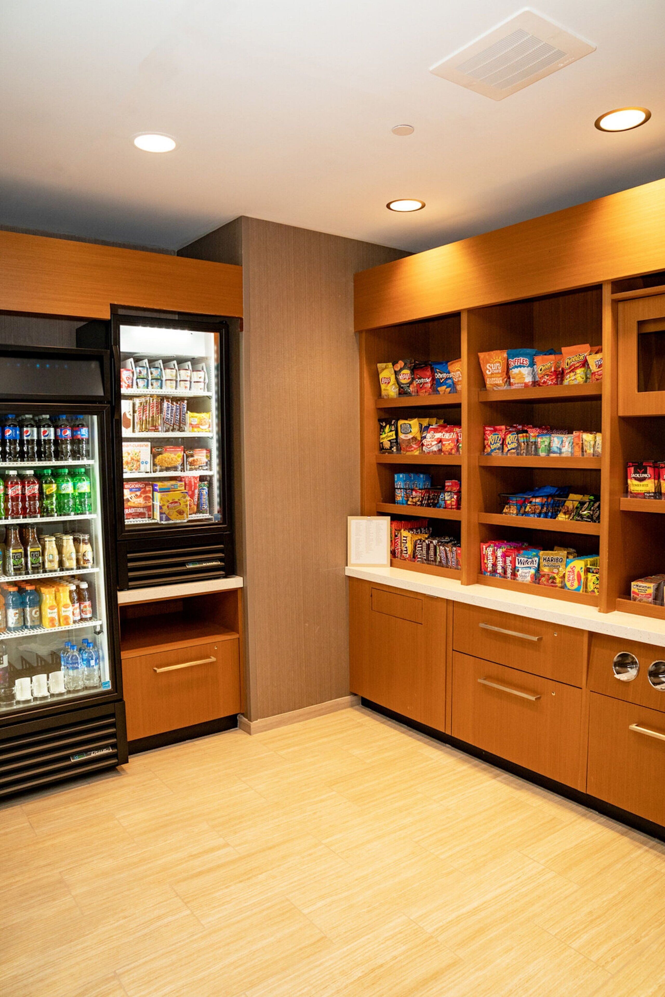 A kitchenette with a refrigerator stocked with beverages and snacks, wooden cabinets, and a countertop.