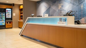 Un espace d’accueil d’hôtel comprenant un comptoir en bois, un kiosque numérique et un réfrigérateur rempli de boissons.