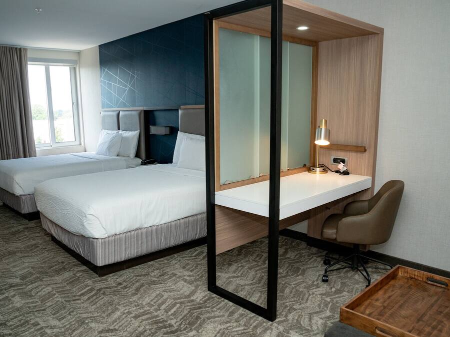 A hotel room with two beds, a desk, a chair, and a small wooden tray.