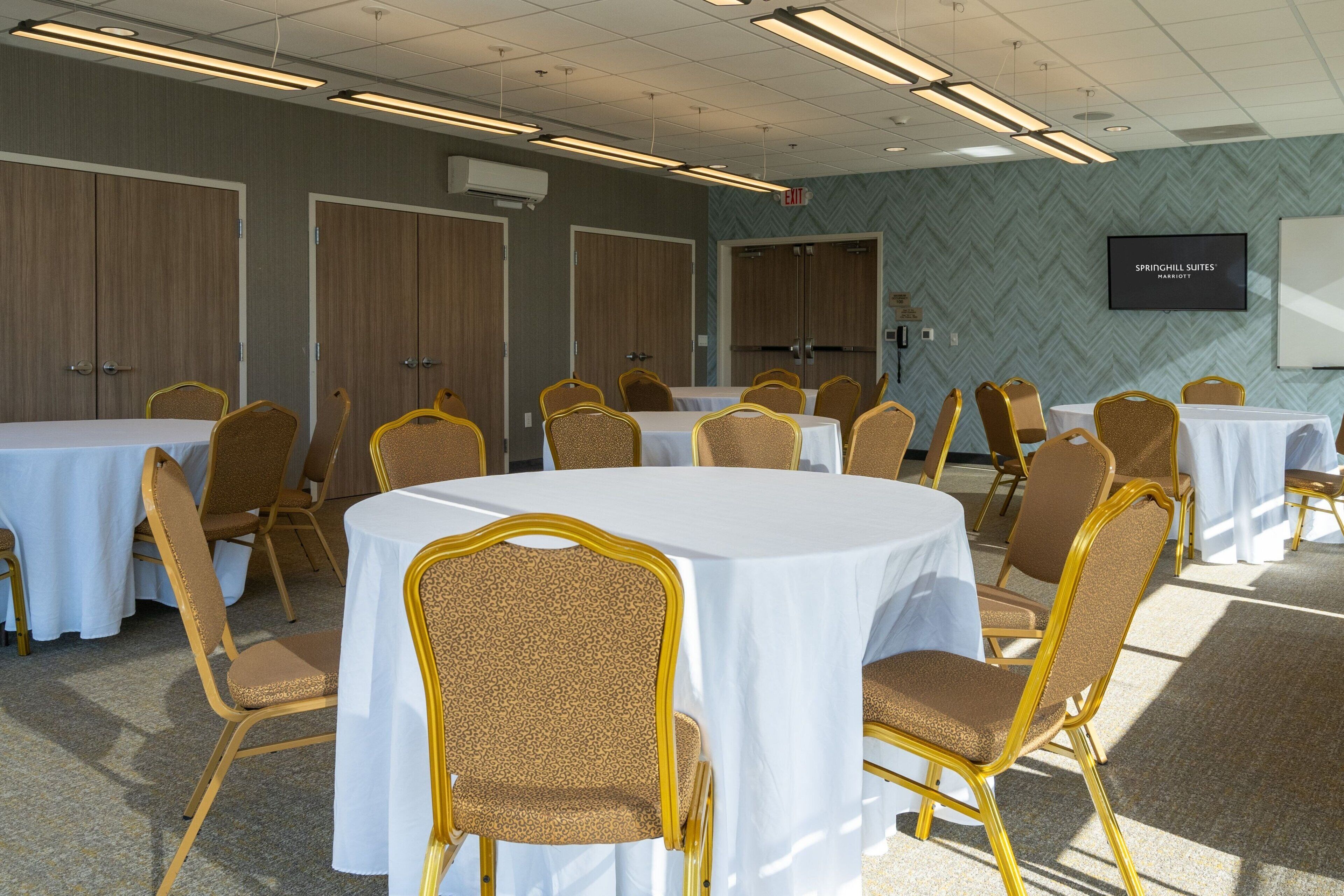A conference room with round tables and chairs, a whiteboard, and an exit sign.