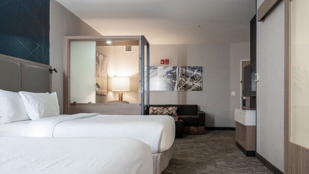 Une chambre d’hôtel avec deux lits, un coin salon, une télévision et une salle de bain visible à travers une porte ouverte.