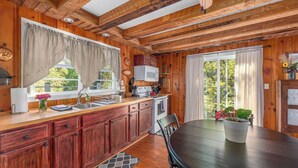 Interior de una cabaña de madera con cocina, comedor y ventanas amplias.