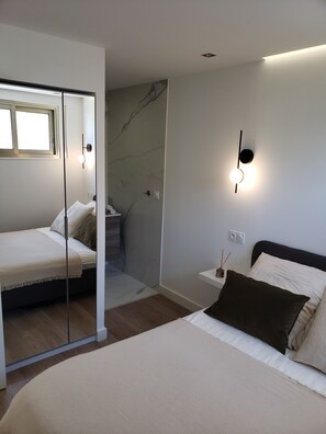 A modern bedroom with a bed, a nightstand, a mirror, and a wall-mounted light fixture. - F2 air-conditioned apartment. 5min Croisette & beaches (Cannes)