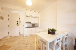 A compact kitchen with white cabinets, a dining table with chairs, and a small plant on the table.