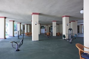 A covered outdoor area with exercise equipment, seating, and pillars.