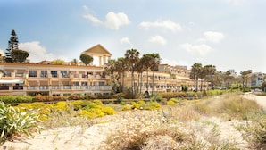 A coastal hotel with multiple balconies, a sandy beach area, and a variety of tropical plants.