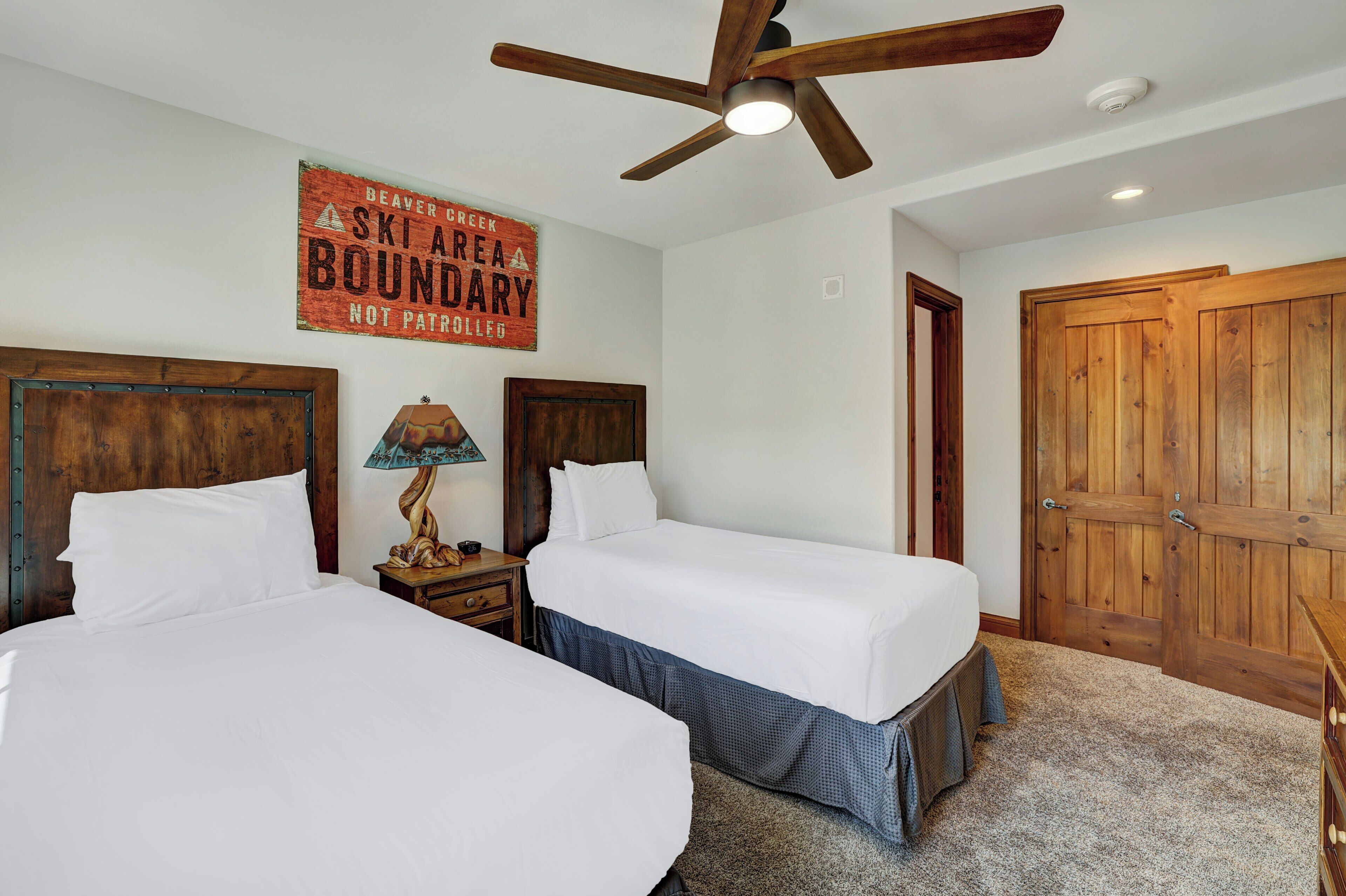 A room with two beds, a ceiling fan, a wooden door, and a wall sign.