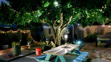 A picnic table with a white tablecloth, surrounded by greenery and string lights.