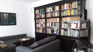 Ein Wohnzimmer mit einem grauen Sofa, einem Bücherregal voller Bücher und einem Bild an der Wand.