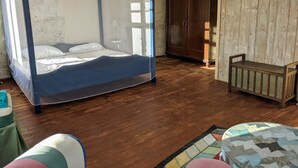 Ein Zimmer mit Himmelbett, Holzschrank, einer kleinen Bank und einem farbenfrohen Teppich.