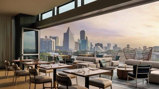 A modern rooftop lounge with a city view, featuring tables, chairs, and a sofa area. - The Tess, Autograph Collection (Atlanta)